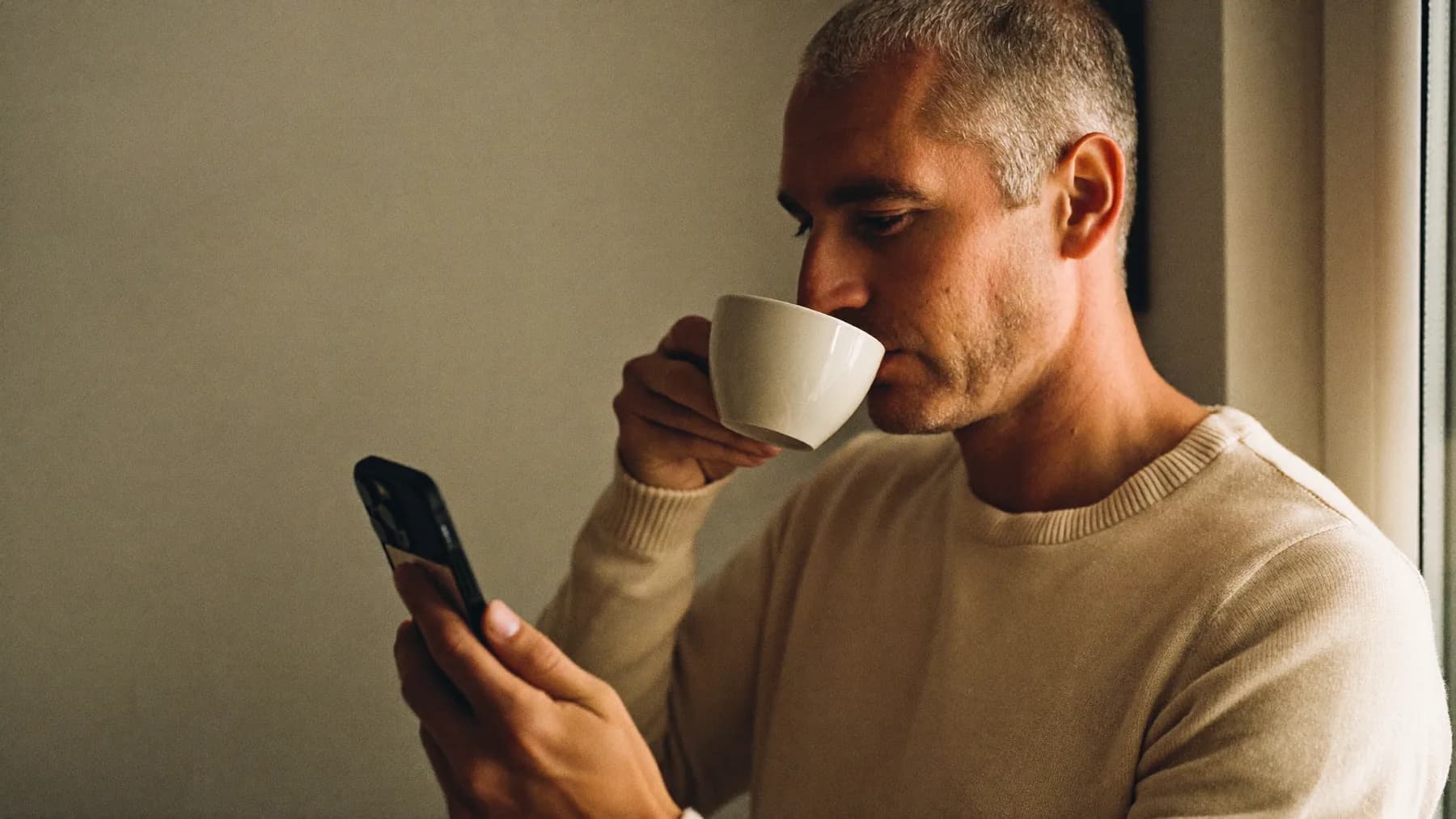 Mężczyzna z telefonem i kawą przy oknie